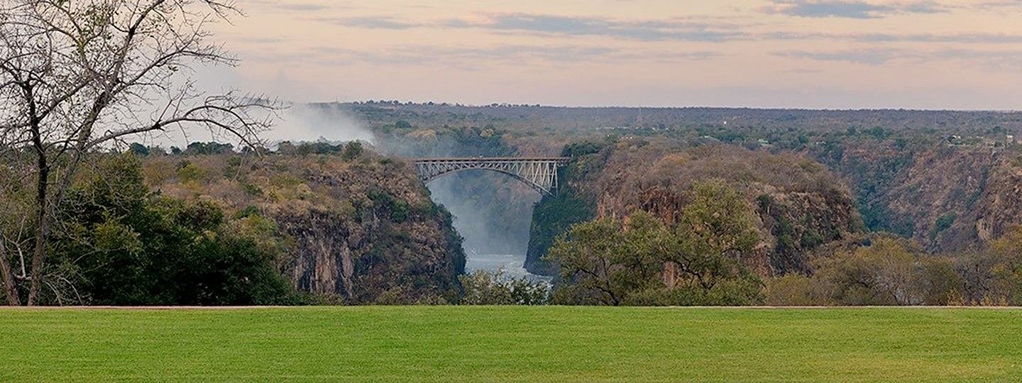 The Victoria Falls Bridge seen across the hotel lawn, with spray rising from the gorge beyond.